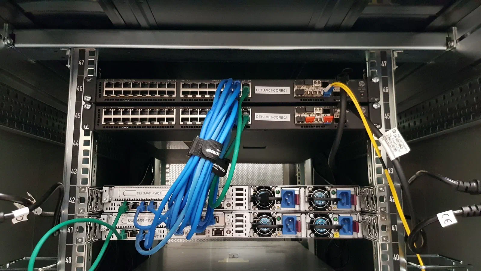 Zwei beschriftete Core-Switches und zwei Firewalls in einem Serverschrank, Netzwerkkabel gebündelt und geführt.